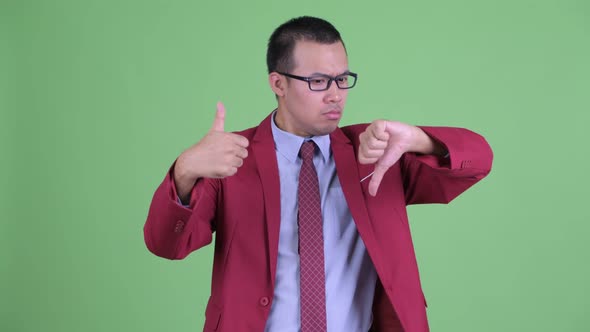 Confused Asian Businessman Choosing Between Thumbs Up and Thumbs Down