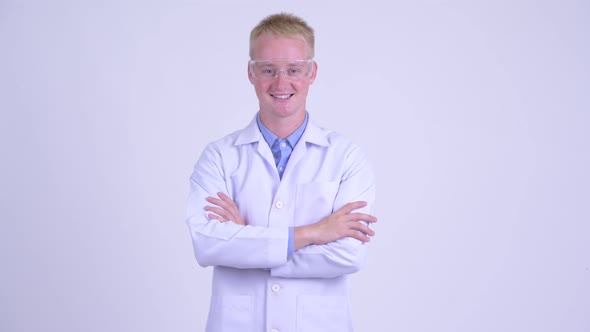 Happy Young Blonde Man Doctor Wearing Protective Glasses with Arms Crossed