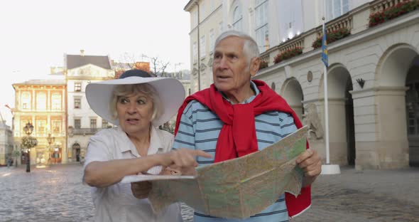 Senior Male and Female Tourists Walking with a Map in Hands Looking for Route