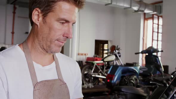 Male mechanic using laptop in motorbike repair garage 4k