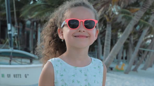 Close-up Portrait of a Beautiful Little Girl in Pink Glasses, Cute Smiling, Looking at the Camera