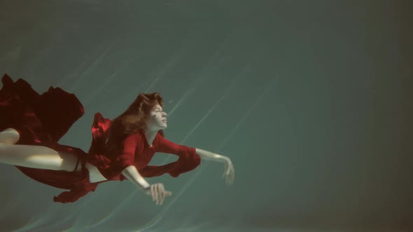 Attractive Redhaired Young Woman Swims Beautifully Underwater in a Red Dress