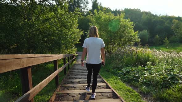 Young Attractive Fit Girl or Woman in White T-shirt and Black Sport Pants Walking Down the Stairs in