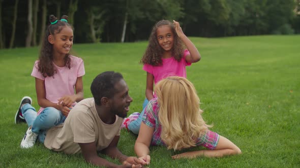 Diverse Parents Lying on Grass with Girls on Back