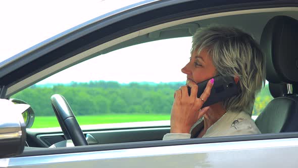 Middle Aged Woman Sits in the Car and Calls with the Smartphone - Car Stands on the Verge of Road