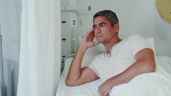 Front view of Caucasian male patient looking away while lying on hospital bed in hospital ward 4k