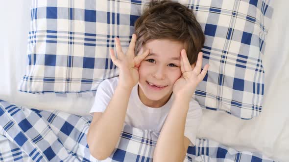 Happy Preschooler Boy Enjoying Comfortable Bedding in Bed Smiling at Camera