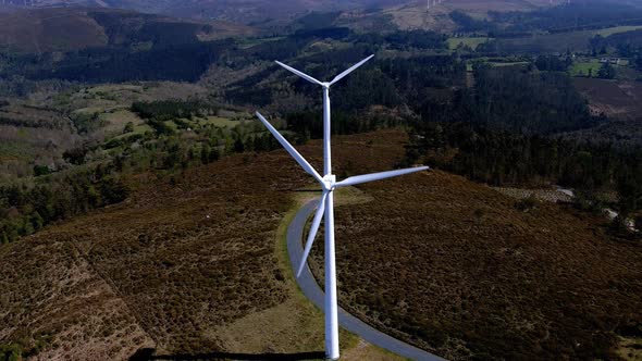 Two wind turbines lined up spinning their blades in the mountains with small green forests of trees