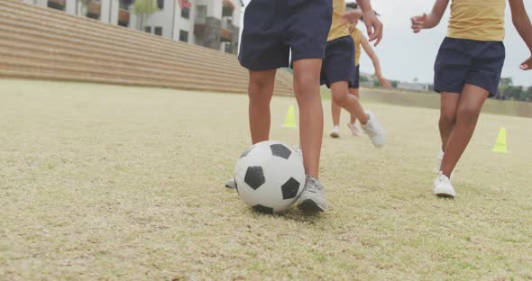 Video of legs of diverse girls playing soccer in front of school