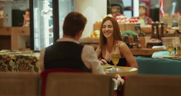 Beautiful Young Woman is Sitting in a Restaurant with a Man Having Fun Talking