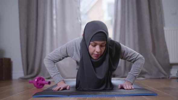 Portrait of Muslim Woman in Hijab Pushing Up at Home. Confident Strong Woman in Sportswear