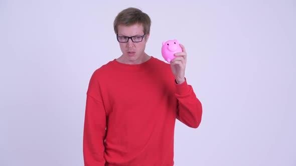 Stressed Young Man Holding Piggy Bank and Giving Thumbs Down