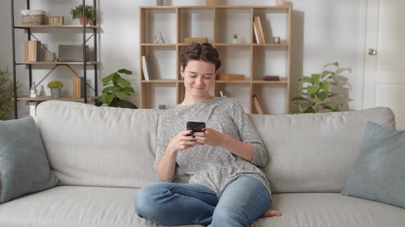 Woman Relaxing on Comfort Couch Using Smart Phone Device Watch Photos Chat in Social Media Network