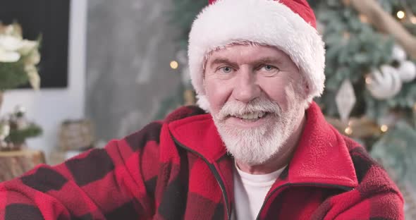 Close-up Portrait of Old Caucasian Man in Red Christmas Hat Looking at Camera and Winking, Positive