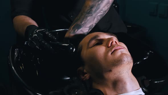 Man Barber in Black Mask Washing His Client Hair in Black Sink