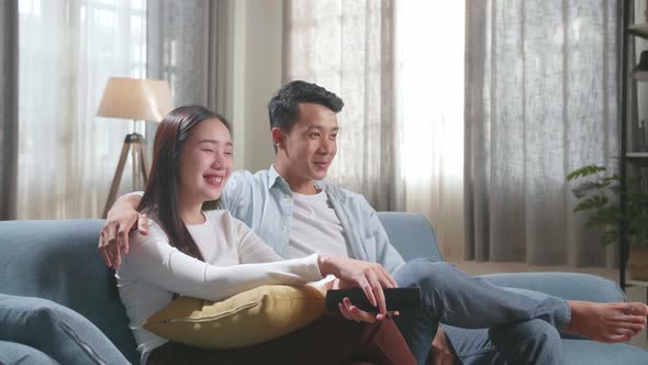 Happy Young Asian Couple Relaxing And Watching Tv At Home