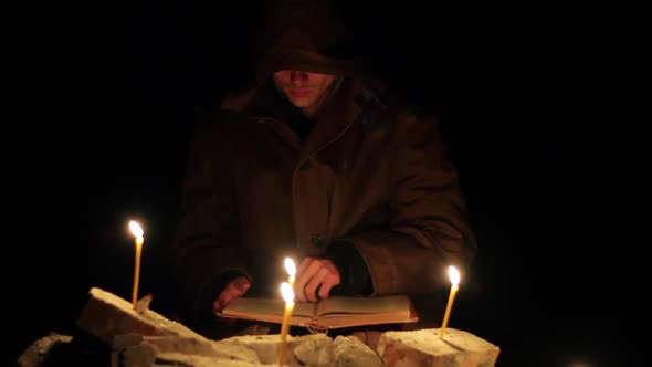 a Man in a Cloak with a Hood is Reading a Hot Book with Candles on the Floor