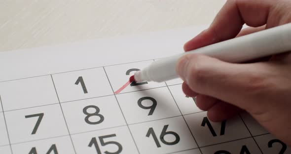 Man's Hand Write Down the 2Th Day on the Paper Calendar Using a Red Pen