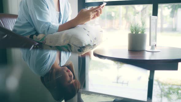 Asian woman using smartphone for talking, reading and texting while sitting on table