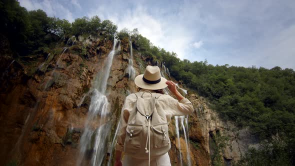 Happy girl at the cascade of the waterfall on the mountain in the park