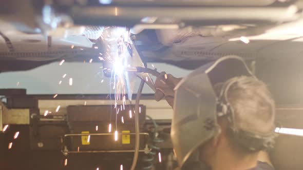 Car service worker welds and repairs an exhaust pipe of a car. Close-up welding 