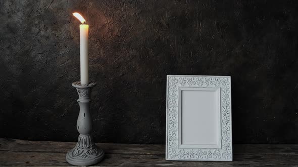 An old photo frame and a burning candle in a retro candle holder.