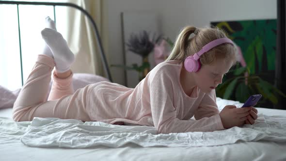 Modern Life of Generation Z. Teenage Girl in Pajamas and Headphones in the Room on the Bed Listens