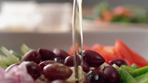 Camera follows pouring olive oil over greek salad. Slow Motion.