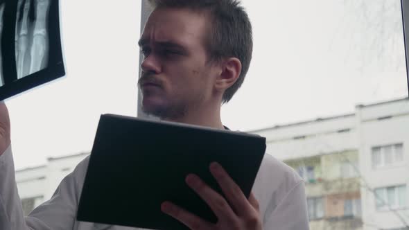 Young doctor looking at a x-ray picture, against the background of a window