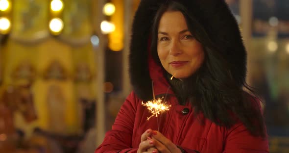 Portrait of Positive Caucasian Woman in Red Coat Holding Sparklers and Smiling. Happy Adult Lady