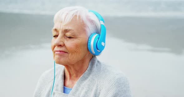 Senior woman listening music on headphone on beach