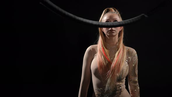 Slim Young Woman in Stage Costume Standing at Black Background Spinning Air Hoop Looking Up