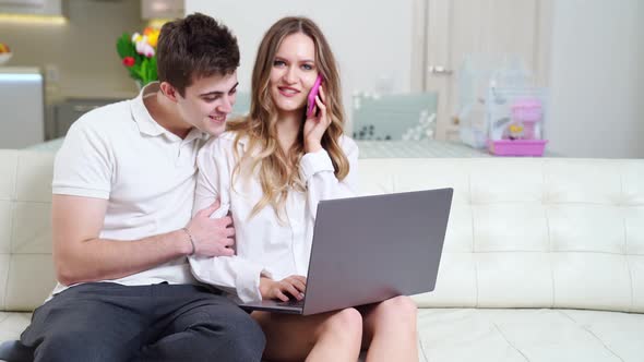 a Man Prevents a Young Beautiful Woman to Work on a Laptop and Talk on the Phone