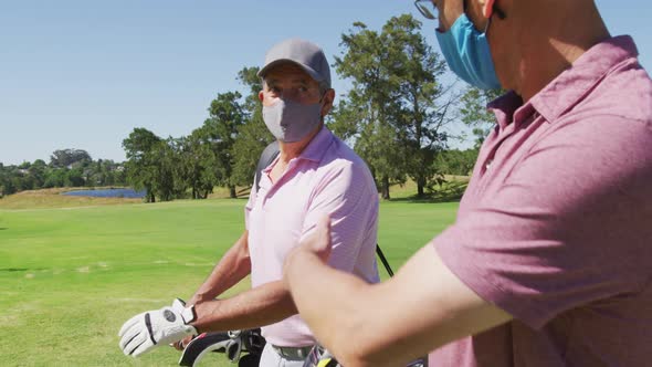 Two caucasian senior man wearing face masks walking with their golf bags at golf course