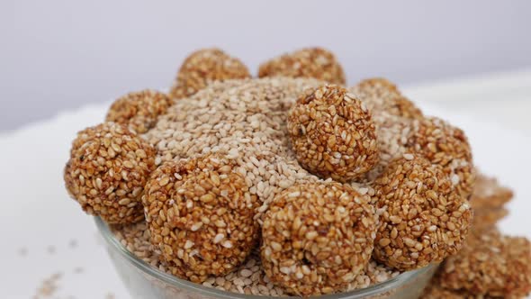 View of dropping sesame ladoo over bowl filled with sesame seeds