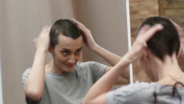 Woman Shakes Off the Remains of Hair After Cutting From Head Standing Near the Mirror in a Gray