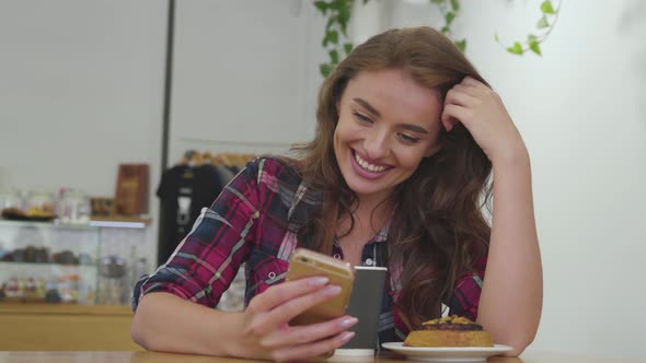 Smiling woman using mobile phone and drinking coffee indoors. 