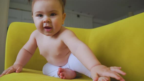 the Portrait of the Baby Girl Playing on the Yellow Sofa at Home in the Living Room