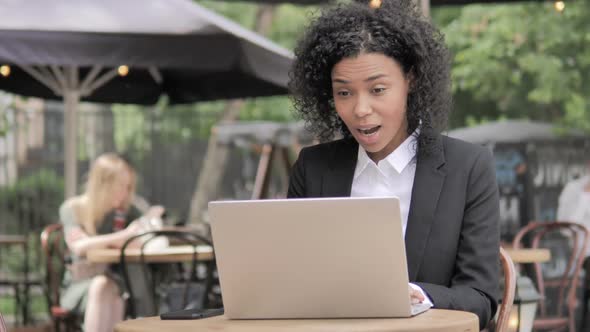 African Businesswoman Celebrating on Laptop in Outdoor Cafe