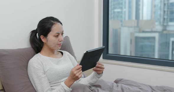 Woman study on tablet computer with apply paper mask on face at home