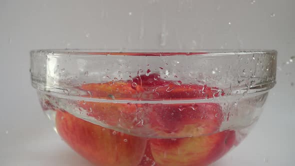 Falling apples in a glass bowl of water. Slow motion.