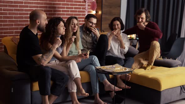 Close Friends are Sitting on the Sofa  Chatting Eating Pizza Smiling