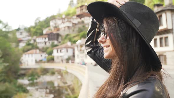 Girl Traveler with Black Hat and Sunglasses Smiling with Old Houses in the Background