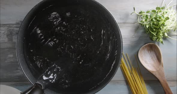 Overhead shot: pouring water in a pot before starting to cook spaghetti pasta.