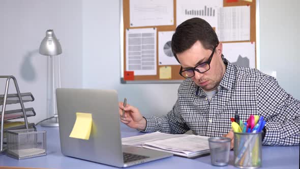 Manager Fills Out Paper Forms in the Workplace and Looks at the Laptop Monitor