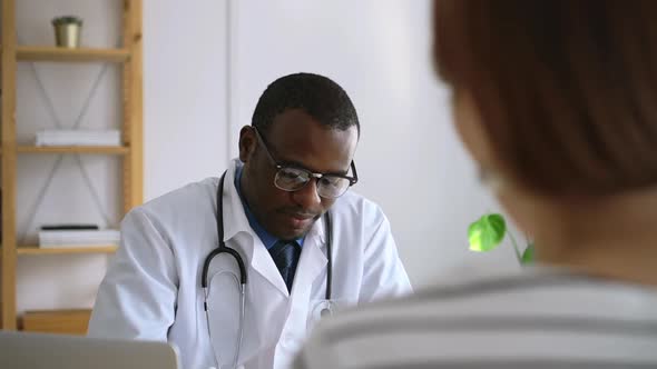 Young Male Doctor is Talking with Female Patient and Writing at Table in Modern Clinic Spbas