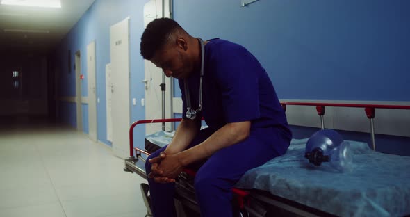 A Doctor Sits on a Medical Gurney in Empty Hospital Corridor