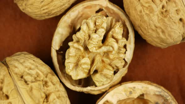 One Opened Walnut Rotates Near Whole Nuts on Brown Background