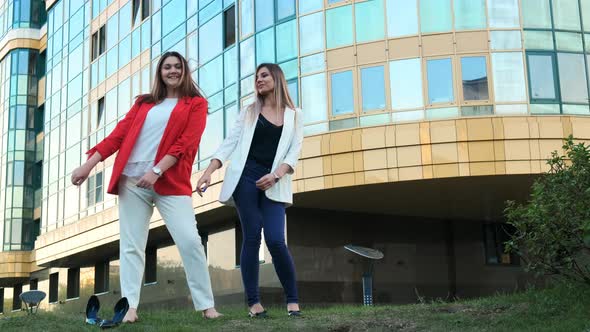 Two Happy Business Women Dancing in the Street Against the Background of a Business Center.