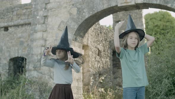 Boy and Girl Standing in Witch Hats Among Stone Walls of Castle